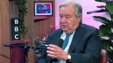 Antonio Guterres gestures as he talks into a microphone with a plant in background during an interview with BBC