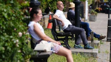 People sit on park benches to soak up the sun in the UK. 