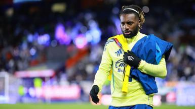 Allan Saint-Maximin walking alongside the pitch. He has black hair, tied back, with blonde tips.