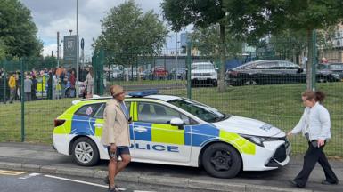 A police car parked outside a school as people walk past. 