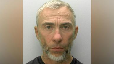 A police mugshot of James Holder. He has cropped grey hair and a short grey beard and is looking directly ahead.