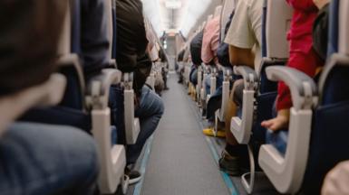 Two rows of seats on a plane featuring many passengers