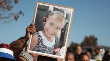 A picture of a young girl who is smiling is held to the sky among a crowd of people.