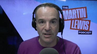 A man, Martin Lewis, has short brown hair and wears a purple jumper. He sits in front of a microphone and is wearing headphones.
