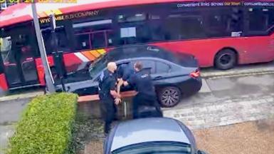 Two police officers are pulling a man out of a BMW crashed into a lamppost near a red bus