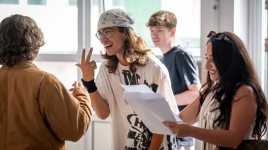 A group of students gather around holding papers and gesturing to each other while reading their results at a high school in Cardiff on Thursday.
