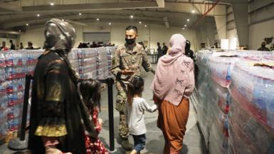 A soldier guides Afghan Special Immigrants. Pictured here are some women and children seen from behind, into the dining facility, August 20, 2021 at Camp As Sayliyah, Qatar