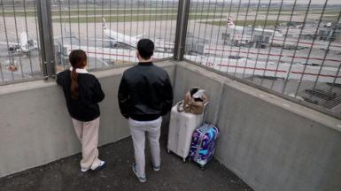 Two passengers looking down on the airport runway where several British Airways branded aeroplanes are standing