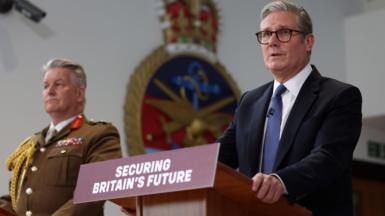 UK Prime Minister Keir Starmer in a suit, accompanied by General Sir Jim Hockenhull in military uniform standing at podiums with a sign that reads 'Securing Britain's Future'