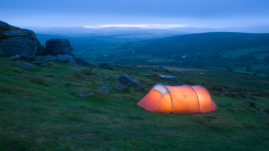 An orange tent lit from inside on Dartmoor moorland at dusk.