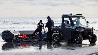 Two French National Police officers stand next to a deflated small boat and a beach buggy as they confiscate the boat after preventing migrants from boarding, on the beach of Gravelines, near Dunkirk, northern France on April 26, 2024.