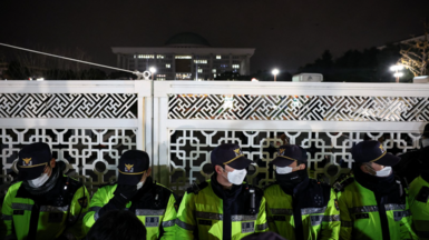 Police in caps, facemasks and high-viz jackets stand guard in front of the gate of the National Assembly after South Korea's president declared martial law