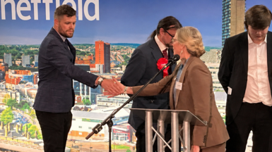 A man in a blue suit shakes the hand of a woman, the counting officer, who congratulates him.