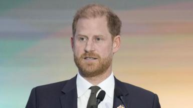 Prince Harry, wearing a dark suit and dark green tie