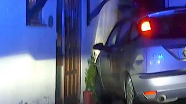 Car resting front-first on the side wall of a house.