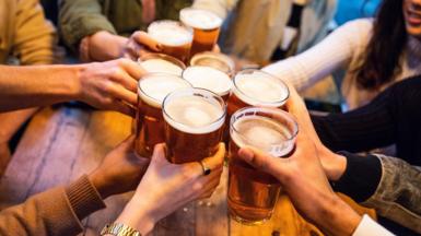 A young group of friends clinking pint glasses of beer together around a pub table