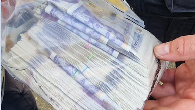 A police officer holds a plastic bag full of £20 notes