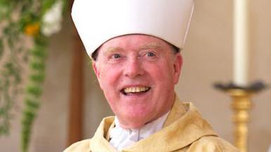 The Right Reverend Thomas McMahon wearing ceremonial attire, including a gold-coloured robe and a large white mitre headgear. He is smiling.