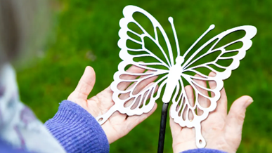 A woman in a purple jumper is holding a large steel butterfly.