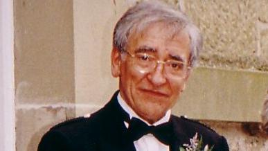 A man in a dark jacket, white shirt and bow tie standing in front of a wall