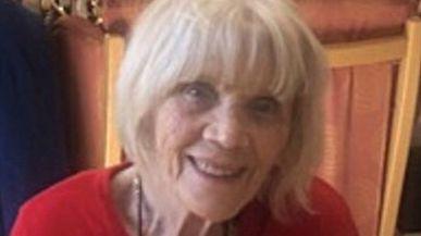 Ruby Harrod, an 88-year-old woman with white hair and a fringe. She is wearing a red top and smiling.