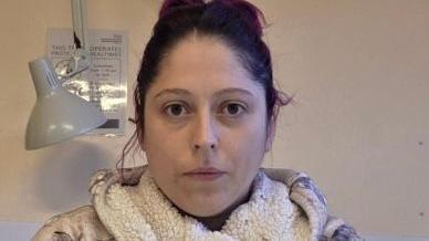 Woman with brown hair wearing a hooded dressing gown. There is a lamp on the wall behind her.