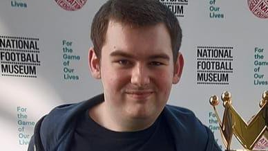 Jack Twydale standing next to the Premier League Trophy in the National Football Museum. He has short dark hair and is smiling with a closed mouth.