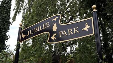 A photograph of an entrance sign at Jubilee Park. It reads "Jubilee Park" in gold lettering on black metal.