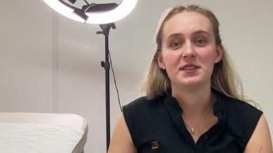 Darcie Rowlandson speaks to camera while sat next to treatment bed and in front of a halo lamp