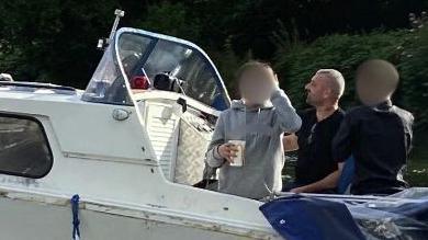 Scott Keen, a shaven headed man, pictured on a power boat with two other men, whose faces are blurred.