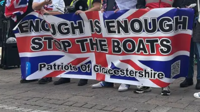 A group of people with Union flags which read "enough is enough" "stop the boats" "Patriots of Gloucestershire"