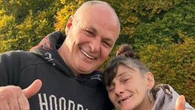 Wayne Putley has a shaved head and is wearing a dark hoodie - his sister has greying hair in a a bun and has a large earring in her left ear.