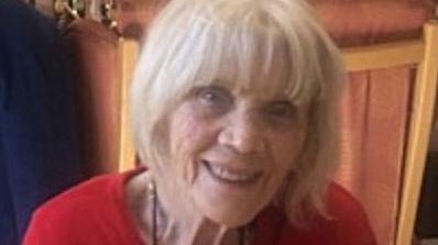 Ruby Harrod, an 88-year-old woman with white hair and a fringe. She is wearing a red top and smiling.