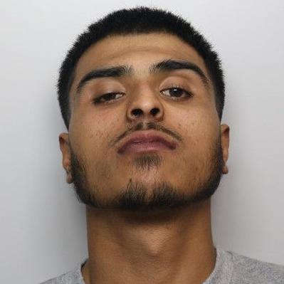 A mugshot of a man with short black hair and black facial hear, wearing a grey top.