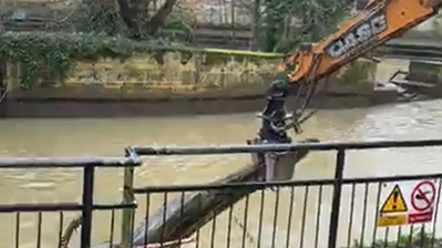 A blurred image of a digger pulling a tree out of a river.