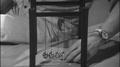 A Newton's cradle, with a hand about to pull back two of the balls.