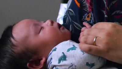 A woman holds a baby in a scene from One Child Nation