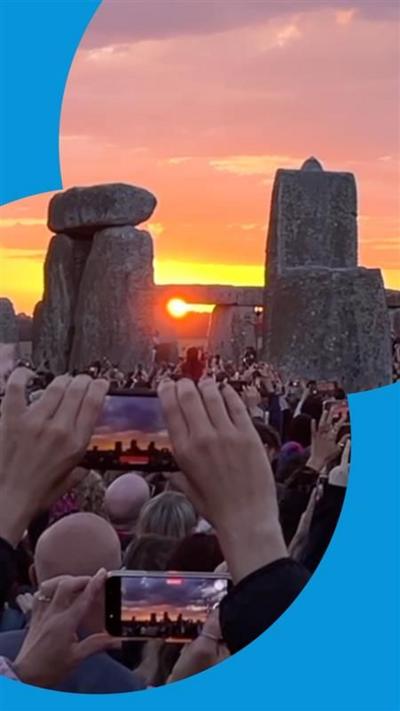 People hold up their phones and filming sun rising over Stonehenge