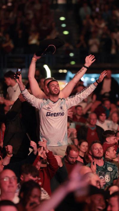 Aston Villa fans in a crowd at utilita arena Birmingham, hands aloft.