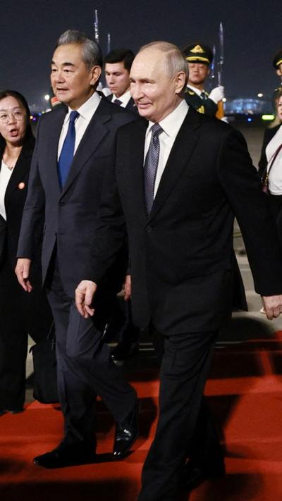 Vladimir Putin and Chinese Foreign Minister Wang Yi walking on red carpet on tarmac at Beijing airport
