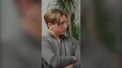 Max Murray sits with his arms crossed. He has blond hair styled as curtains and wears a grey top 