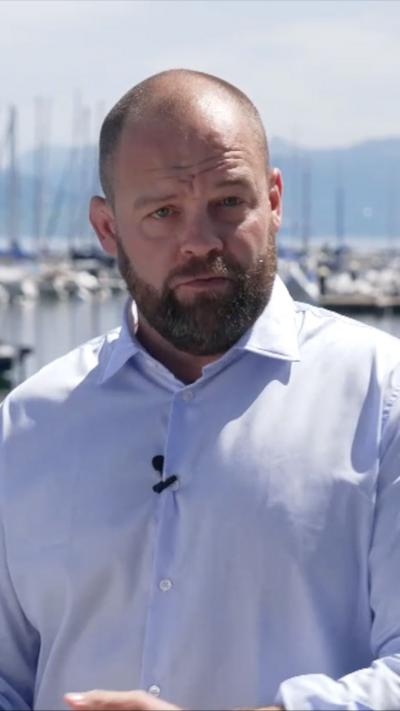 James Waterhouse standing by a docking area in Switzerland - he is wearing a blue shirt and has cropped hair