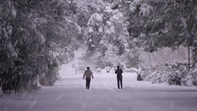 Migrants walking along snowy Greek road.