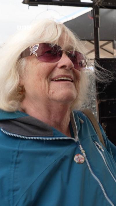 A woman with white hair, sunglasses and a blue coat