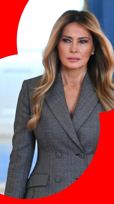 Melania walking towards camera, looking away from the lense, wearing a grey blazer. 