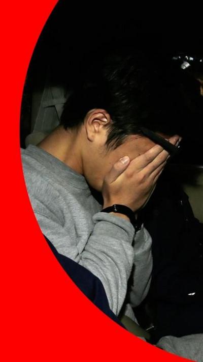Takahiro Shiraishi with his hands over his face, in the back of a police car