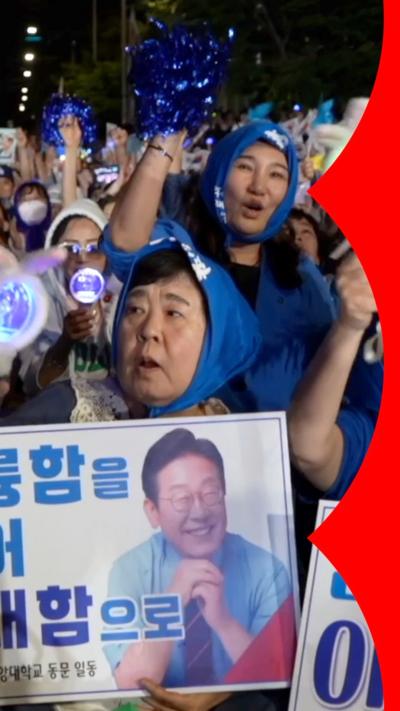 A crowd in Seoul - women wear blue headscarves and hold up blue pom poms and posters of Lee Jae-myung
