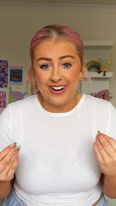 Head and shoulder shot of woman with pink hair tied back wearing white T-shirt
