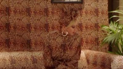 Mandy sits on a sofa. Her leopard print outfit matches it so she blends in.