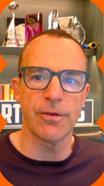 Martin Lewis wears glasses and a purple top. He sits in front of bookshelves